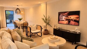 Un salon moderne comprenant un canapé, des fauteuils, un coin repas et un téléviseur fixé au mur.
