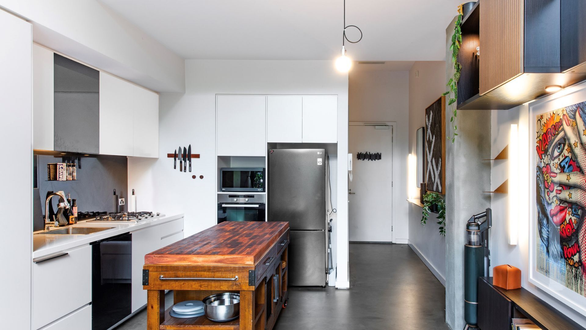 Una cocina moderna con armarios blancos, una mesa de comedor de madera, electrodomésticos de acero inoxidable y un soporte de cuchillos en la pared.