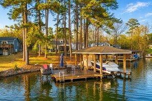 A dock with a covered seating area, a boat, and a house in the background.