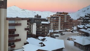 A snow-covered urban area with modern buildings, a parking lot, and a mountain in the background. - Apartment '6 Couchages Val Thorens' with Mountain View, Balcony and Wi-Fi (Val Thorens)