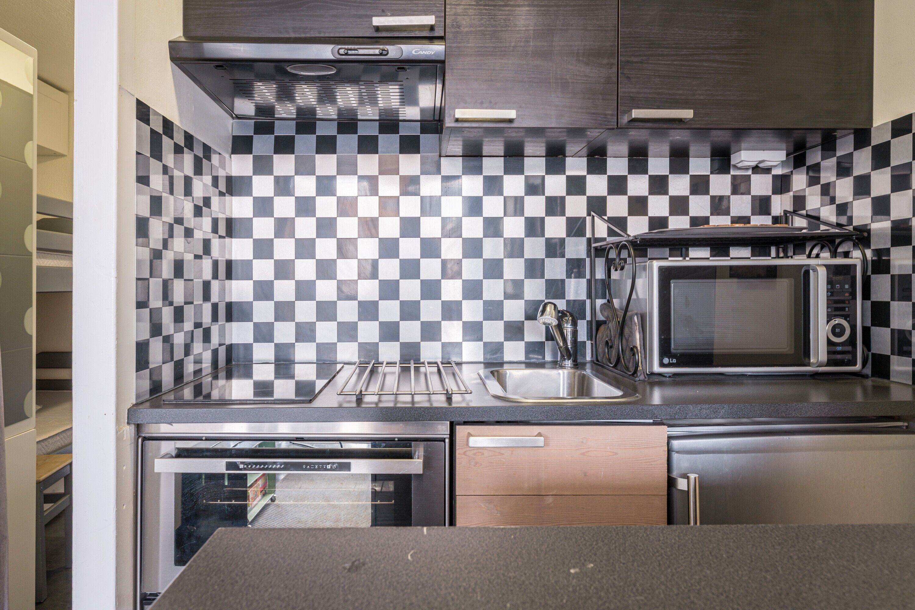 A compact kitchen with a microwave, oven, and checkered backsplash.