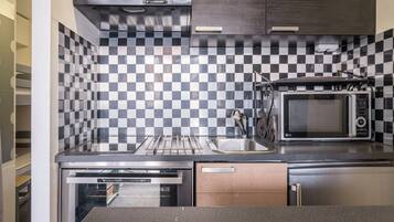 A compact kitchen with a microwave, oven, and checkered backsplash.