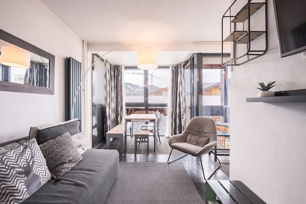 Une pièce moderne comprenant un canapé, un fauteuil, une table à manger et donnant sur l’extérieur.