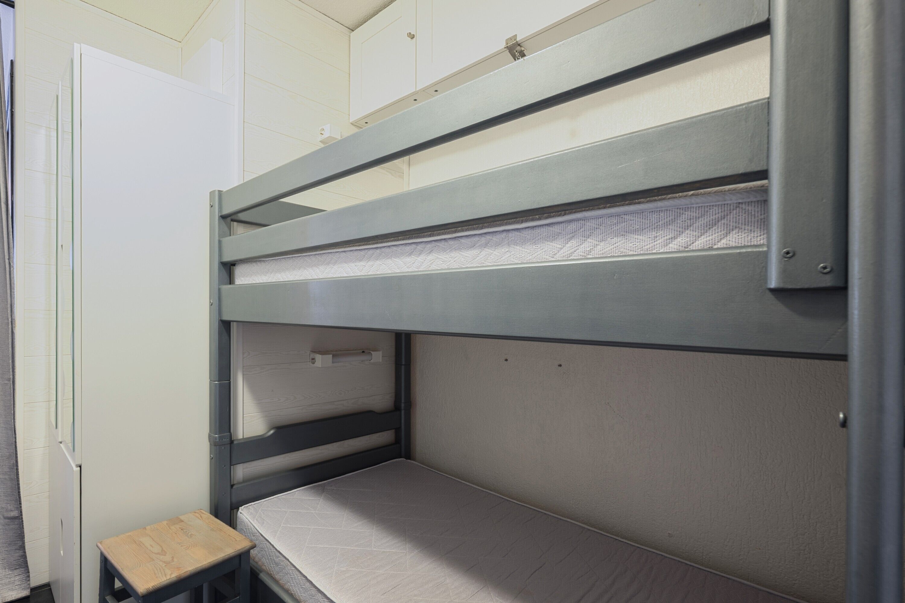 Ein Stockbett mit einer kleinen Holzbank, einer weißen Tür und einer weißen Wand.