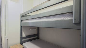 Ein Stockbett mit einer kleinen Holzbank, einer weißen Tür und einer weißen Wand.