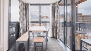 A balcony with a table and chairs, a view of buildings and mountains, and a glass door. - Apartment '6 Couchages Val Thorens' with Mountain View, Balcony and Wi-Fi (Val Thorens)