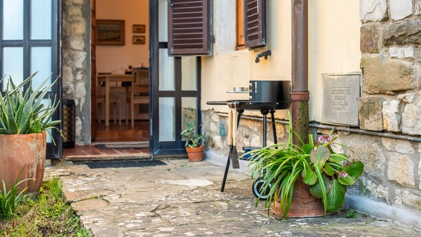 A stone-paved entrance with a grill, potted plants, and a door leading to an interior space.