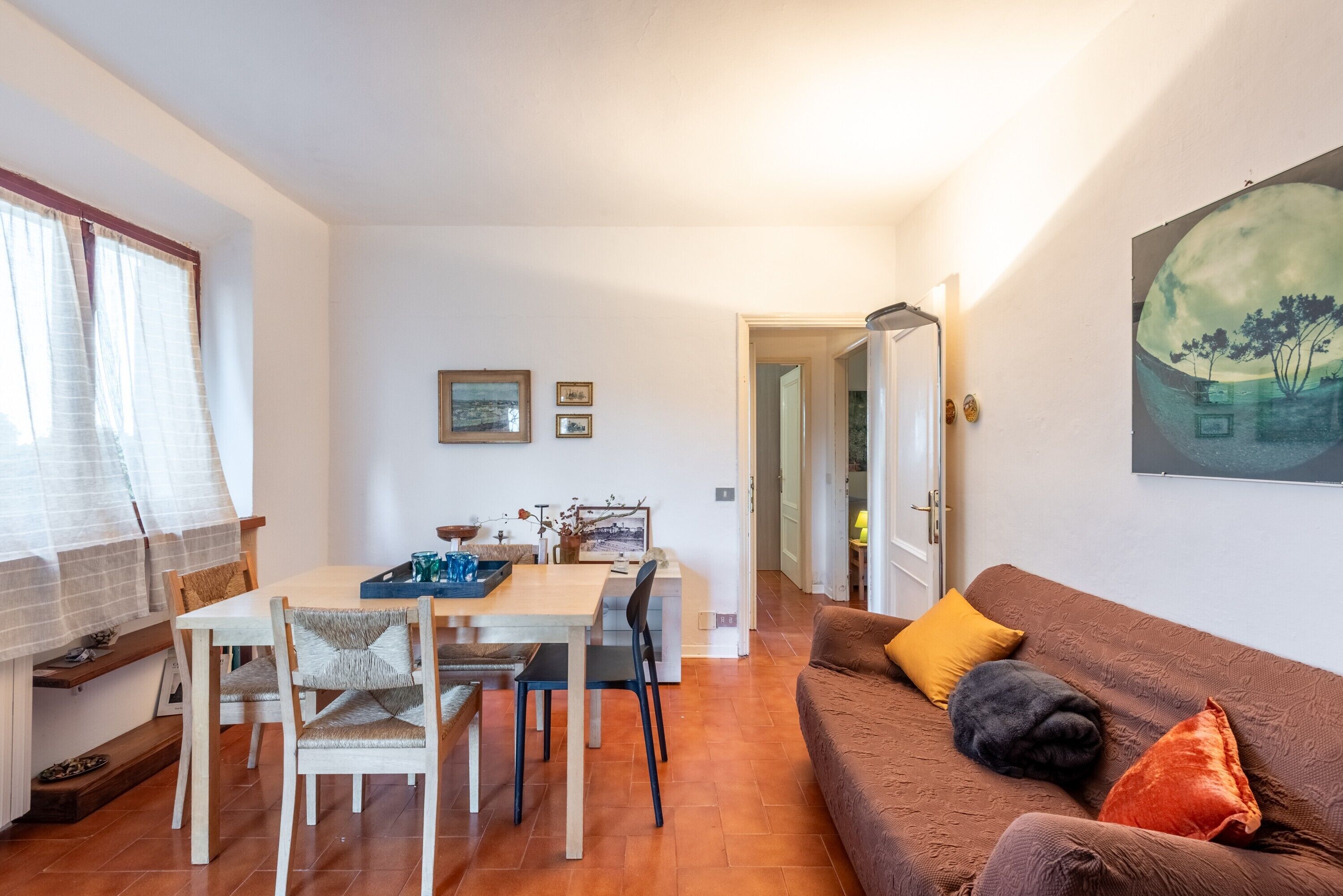 A dining area with a table and chairs, a sofa with cushions, and a painting on the wall.