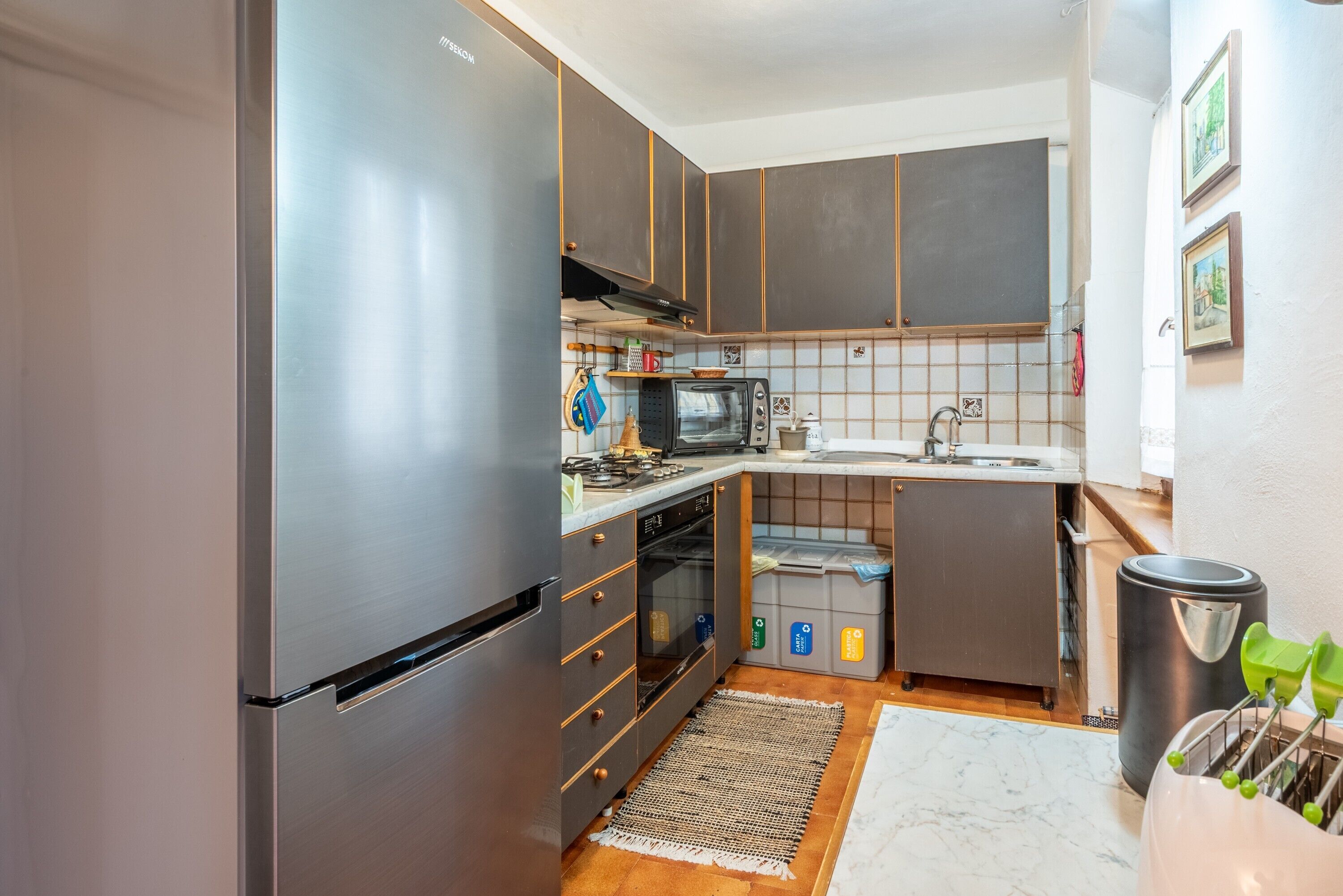 A compact kitchen with a refrigerator, oven, microwave, sink, and a trash bin.