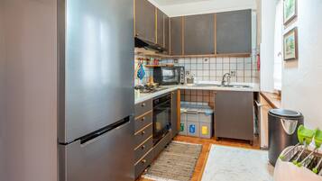 A compact kitchen with a refrigerator, oven, microwave, sink, and a trash bin.
