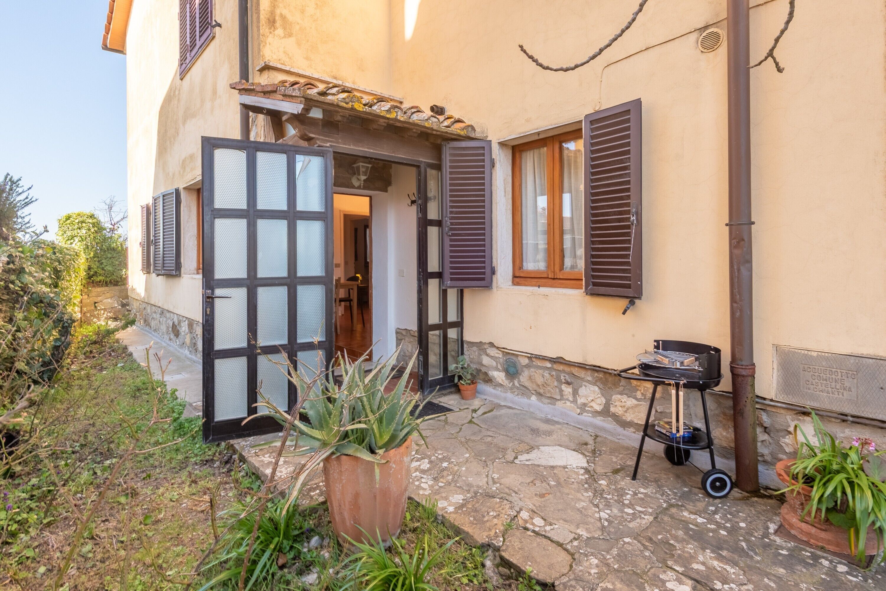 Un pati empedrat amb una planta en test, una barbacoa i una porta que dona a una habitació.