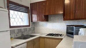 Een keuken met een gasfornuis, een ingebouwde oven, een vaatwasser, houten kastjes, een spoelbak en betegelde spatwand.