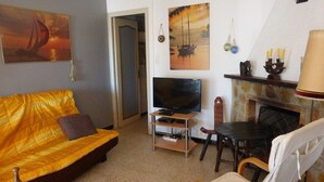 Een woonkamer met een bank, televisie, open haard en kunstwerken aan de muur.