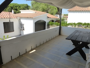 Eine Terrasse mit Tisch und Stühlen, eine weiße Wand und ein Ziegeldach.