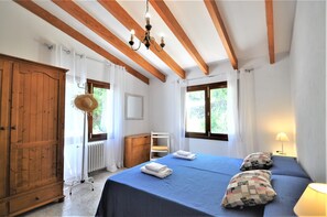 Un dormitorio con dos camas, vigas de madera, un candelabro, un radiador y una ventana con cortinas.
