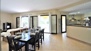 Un comedor con una mesa preparada para cuatro, una cocina con estufa y fregadero, y un ventanal corredizo que da a un espacio exterior.