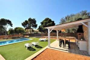 Ein Garten mit Swimmingpool, weißen Liegestühlen, Grillplatz und einer Pergola.