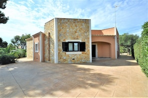 A modern building with a stone facade, a central window, and a paved entrance area.