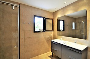 Ein modernes Badezimmer mit Glasdusche, großem Spiegel und Waschtisch mit Becken und Schrank.