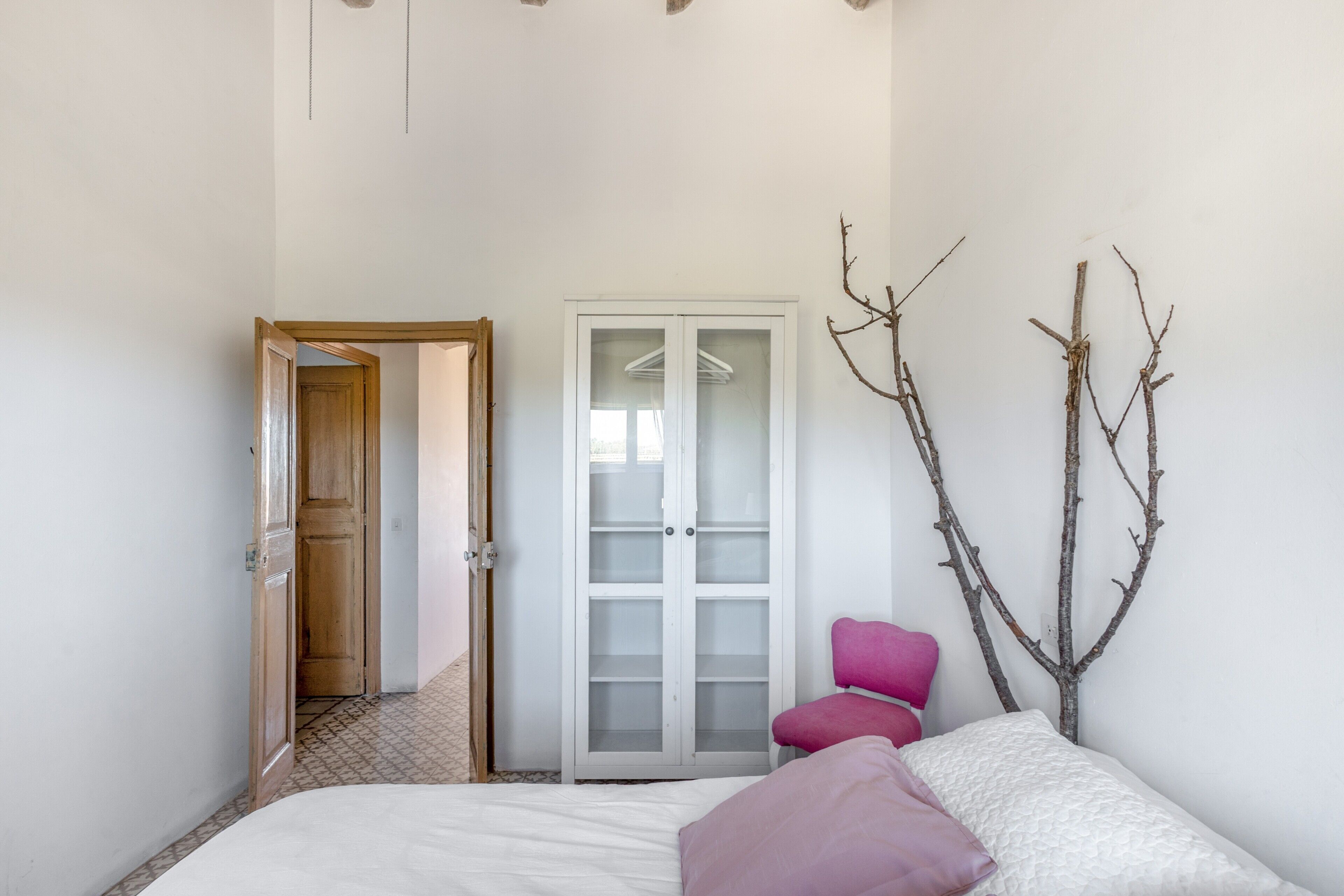 A bedroom with a bed, a wardrobe, a chair, and a door leading to another room.