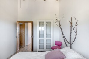 A bedroom with a bed, a wardrobe, a chair, and a door leading to another room.