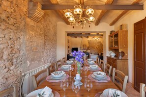 A dining area with a stone wall, wooden ceiling beams, and a chandelier.