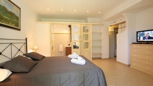A bedroom with a bed, a television, a dresser, and a bathroom visible through an open door. - Country House 'Ca Na Barbara' with Private Pool, Wi-Fi, and Air Conditioning (Santanyí)