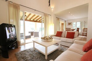 Een woonkamer met een televisie, witte banken, een salontafel en een eethoek met stoelen en een tafel.