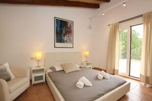 Een slaapkamer met een bed, twee nachtkastjes, een schilderij en een groot raam met gordijnen.