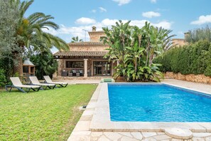 A pool with lounge chairs, a stone building, and tropical vegetation.