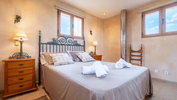 Una cama bien hecha con almohadas y toallas, un aparador de madera, dos lámparas de pared y una ventana con vistas.
