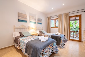 A bedroom with two beds, a nightstand, a lamp, and a view of the outdoors.