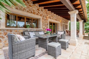 An outdoor patio with wicker furniture, stone walls, and a pergola. - Country House 'Casa Brava' with Private Pool, Wi-Fi and Air Conditioning (Santanyí)