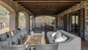 An outdoor patio with stone arches, a wooden ceiling, and a seating area with sofas and chairs.