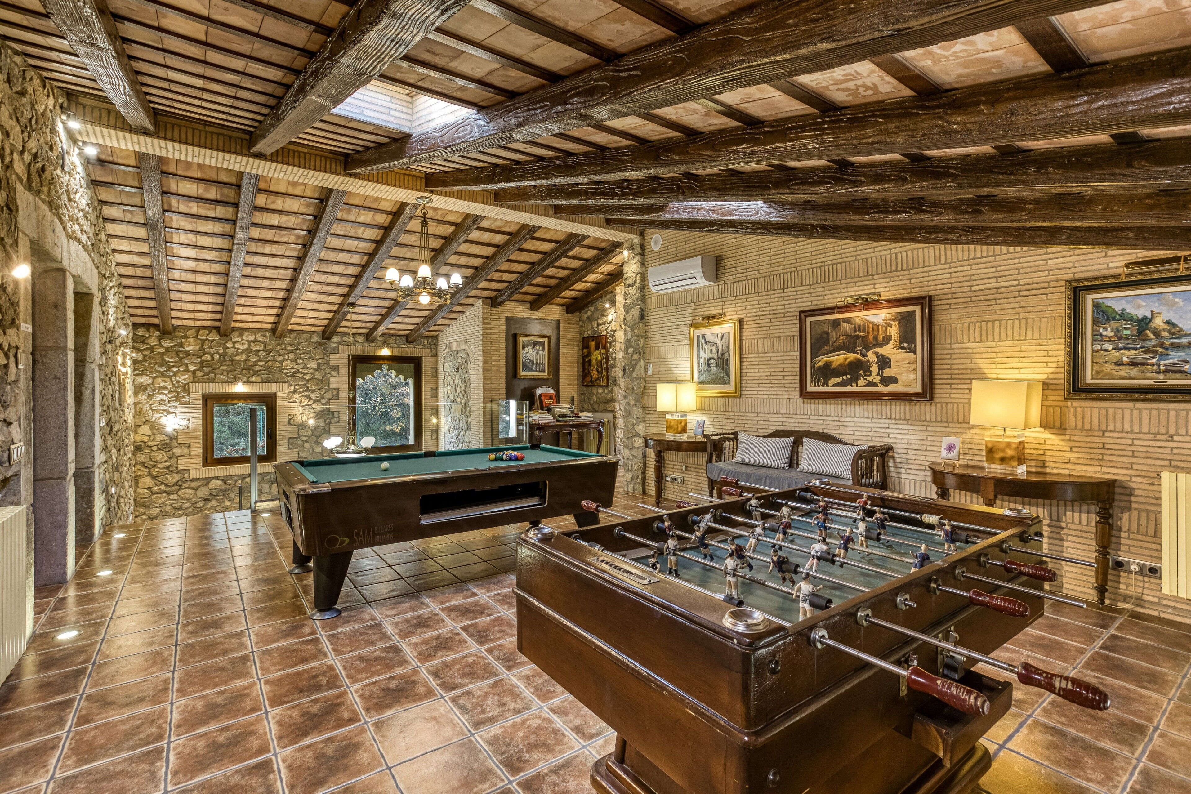 A room with a pool table, foosball table, stone walls, wooden beams, and artwork.