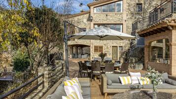 A stone building with a patio area featuring wicker furniture, a dining table, and an umbrella.
