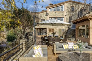 A stone building with a patio area featuring wicker furniture, a dining table, and an umbrella.