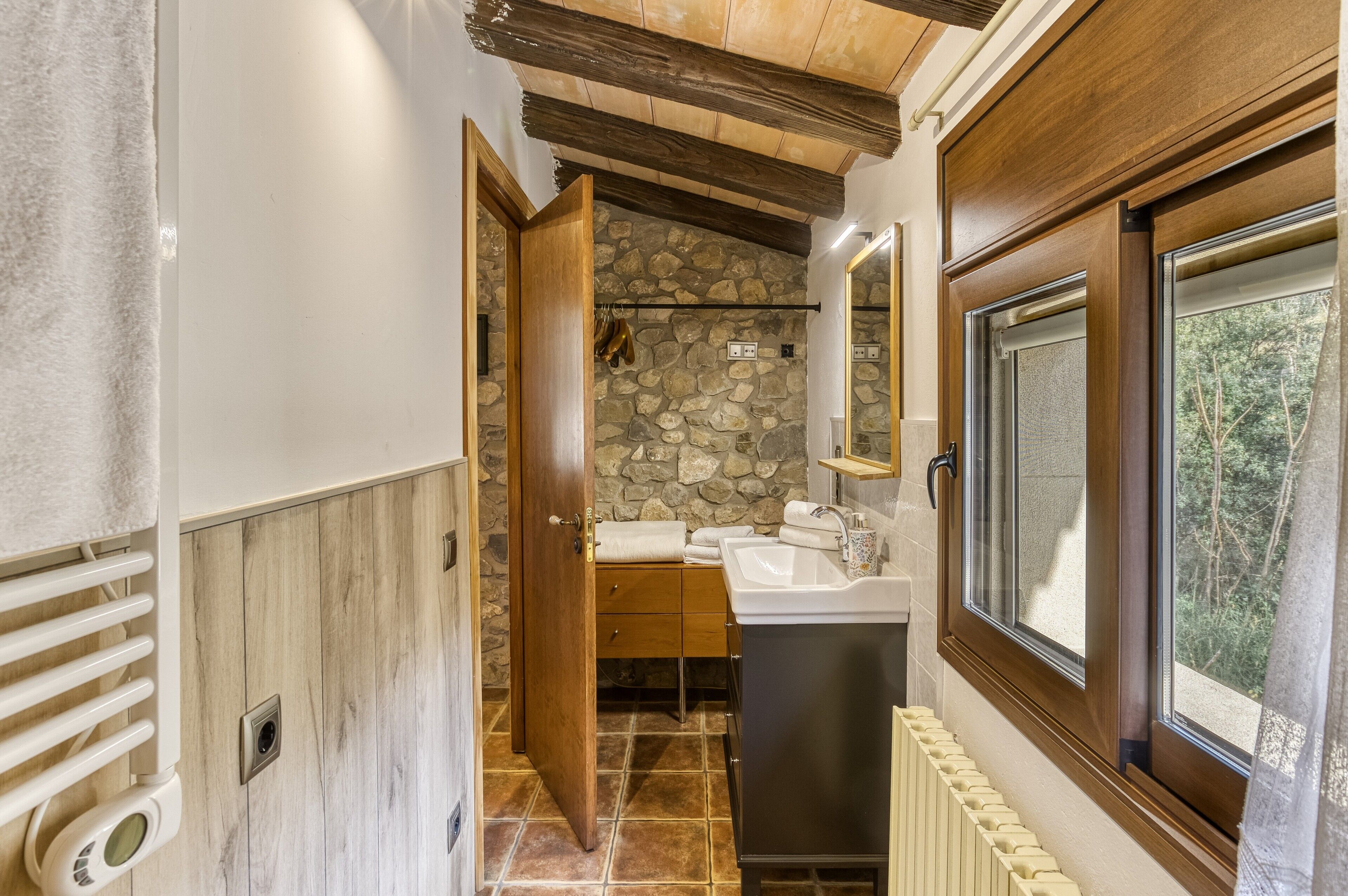 Ein Badezimmer mit Steinwand, Holztür und Fenster mit Blick auf Bäume.