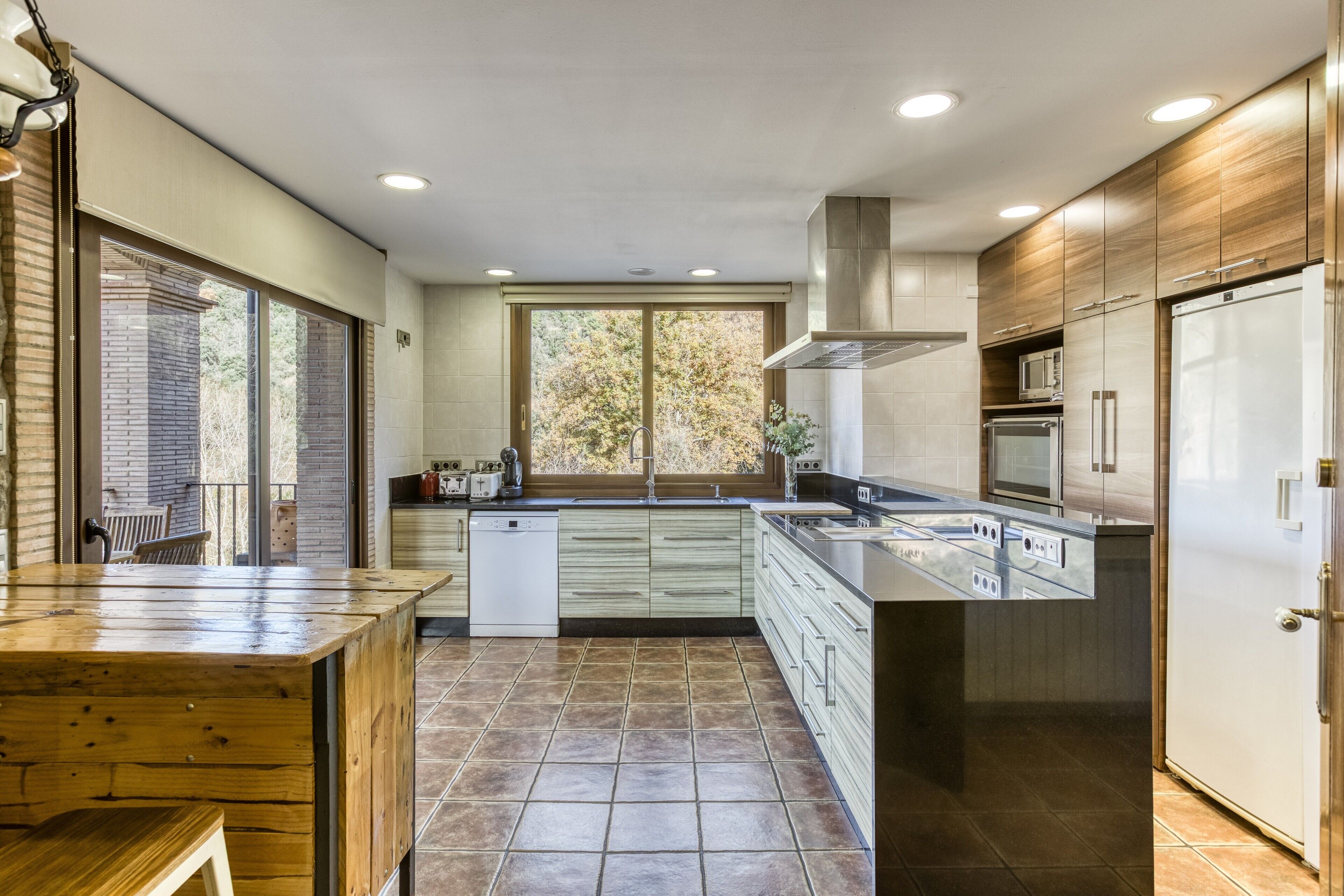 A modern kitchen with a wooden island, stainless steel appliances, and a view of the outdoors.