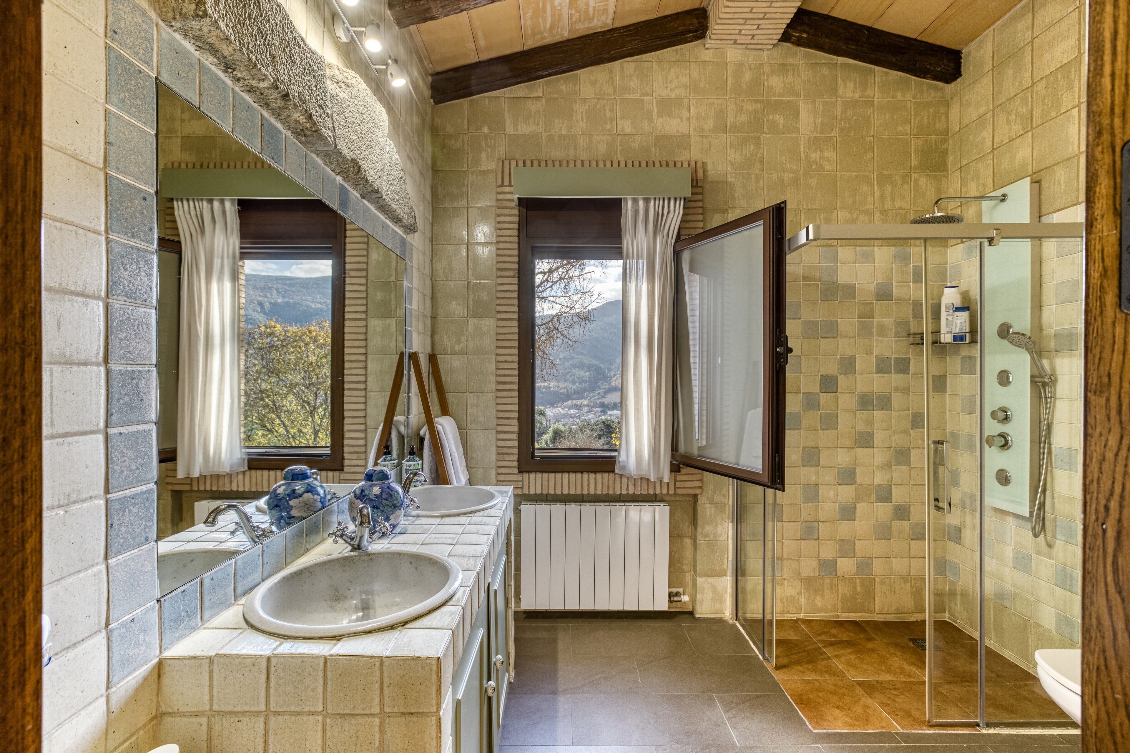Ein Badezimmer mit zwei Waschbecken, einer Dusche und Ausblick durch die Fenster.