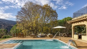 A pool with a waterfall feature, outdoor seating, and a view of trees and mountains.