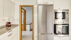 Uma cozinha com armários brancos, uma geladeira de aço inoxidável, um micro-ondas e um forno.