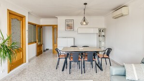 Uma sala de jantar com uma mesa e cadeiras de madeira, um lustre pendurado e um aparelho de ar condicionado branco na parede.