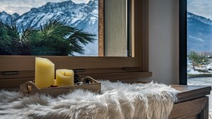A wooden dresser with a fur throw, a window with a view of snow-capped mountains, and two candles in a wooden box. - Apartment 'Rododendro' with Mountain View, Wi-Fi and Air Conditioning (Cavedago)