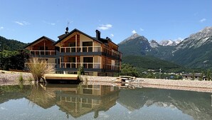 A multi-story wooden building with a clear reflection in a shallow water body, surrounded by mountains. - Apartment 'Rododendro' with Mountain View, Wi-Fi and Air Conditioning (Cavedago)