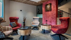Ein modernes Wohnzimmer mit drei roten Polsterstühlen, zwei runden Holztischen und einer Treppe im Hintergrund.