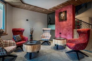 A modern living room with three red upholstered chairs, two round wooden tables, and a staircase in the background.