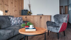 A modern living room with a wooden wall, a grey sofa, a red and grey armchair, a wooden coffee table, and a small decorative plant.