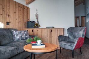 Un salon moderne avec un mur en bois, un canapé gris, un fauteuil rouge et gris, une table basse en bois et une petite plante décorative.