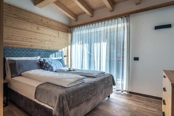 A bedroom with a bed, wooden ceiling beams, a window with curtains, and a bedside table. - Apartment 'Stella Alpina' with Mountain View, Wi-Fi and Air Conditioning (Cavedago)